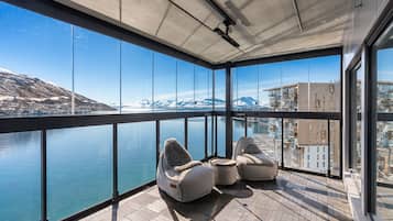 A balcony with a view of a body of water and mountains, furnished with two bean bag chairs and a small table.