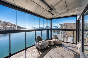 A balcony with a view of a body of water and mountains, furnished with two bean bag chairs and a small table. - Eight floor Premium Waterfront Penthouse (Tromsø)