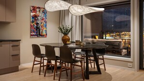 Un comedor moderno con una mesa redonda, sillas, un florero con flores y vistas a la ciudad a través de un gran ventanal.