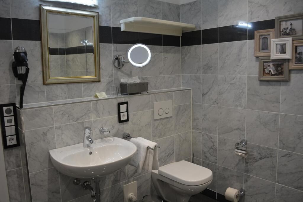 Un baño con lavamanos, inodoro, espejo y cuadros en la pared.
