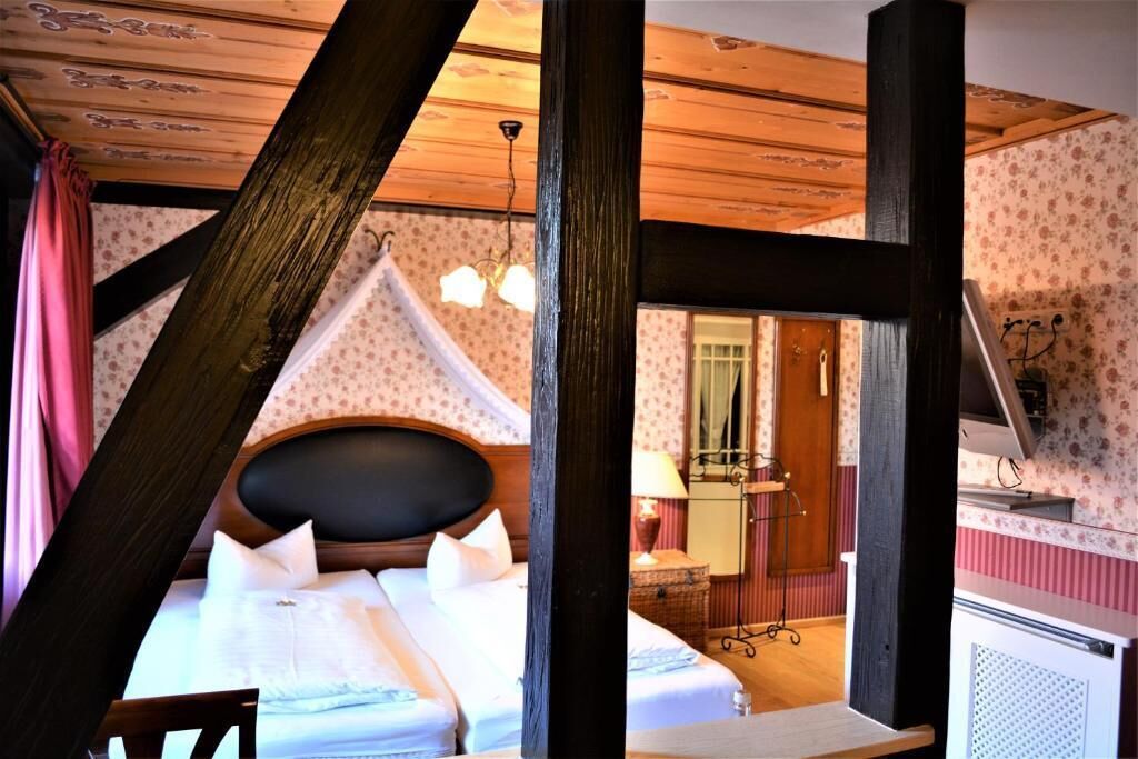 A bedroom with a bed, wooden beams, a chandelier, and a mirror.