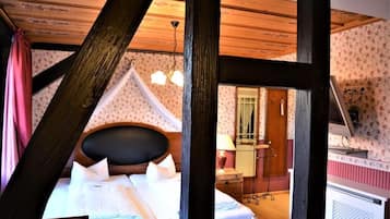 A bedroom with a bed, wooden beams, a chandelier, and a mirror.