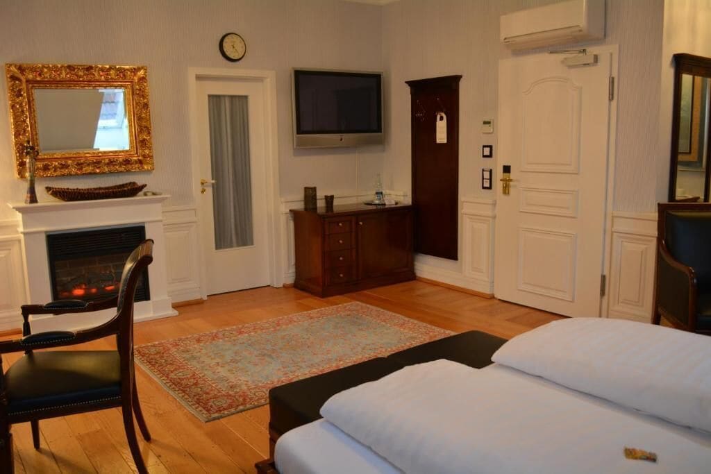 A hotel room with a fireplace, a television, a bed, a desk, and a wardrobe.