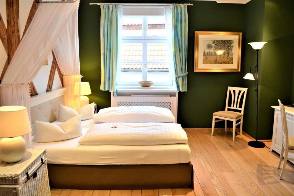 A bedroom with a bed, bedside lamps, a chair, a window with curtains, and a framed picture on the wall.