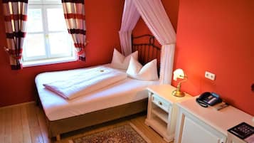 Un dormitorio con cama, mesita de noche, lámpara, teléfono y ventana con cortinas.