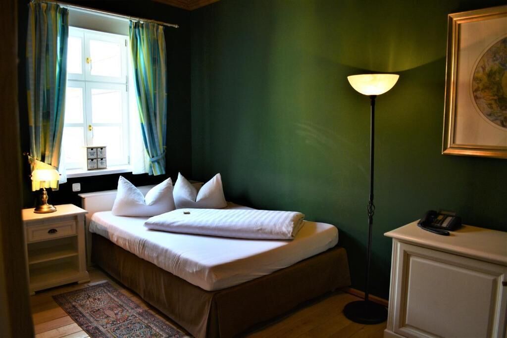 Ein Schlafzimmer mit einem Bett, einem Nachttisch, einer Lampe und einem Fenster mit Vorhängen.