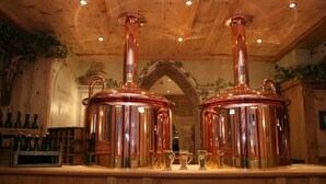 Una zona de bar con hervidores de cobre, vasos y botellas en estantes.