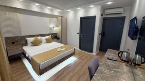 Habitación de hotel con cama, mesita de noche, lámpara, armario, escritorio, silla y cafetera.