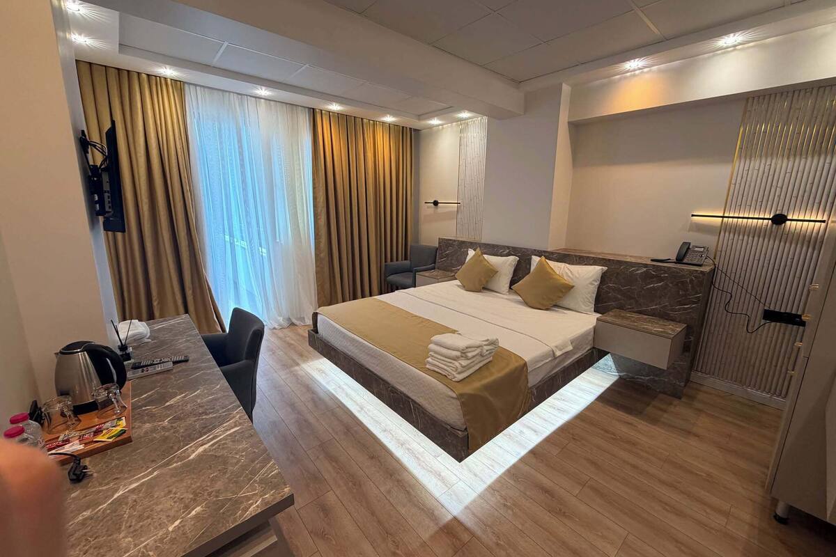 Una habitación de hotel con una cama, mesitas de noche, un escritorio con hervidor y un armario.