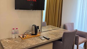 Habitación de hotel con televisión de pantalla plana mostrando Netflix, un escritorio de mármol, dos sillas, cafetera y un refrigerador pequeño.
