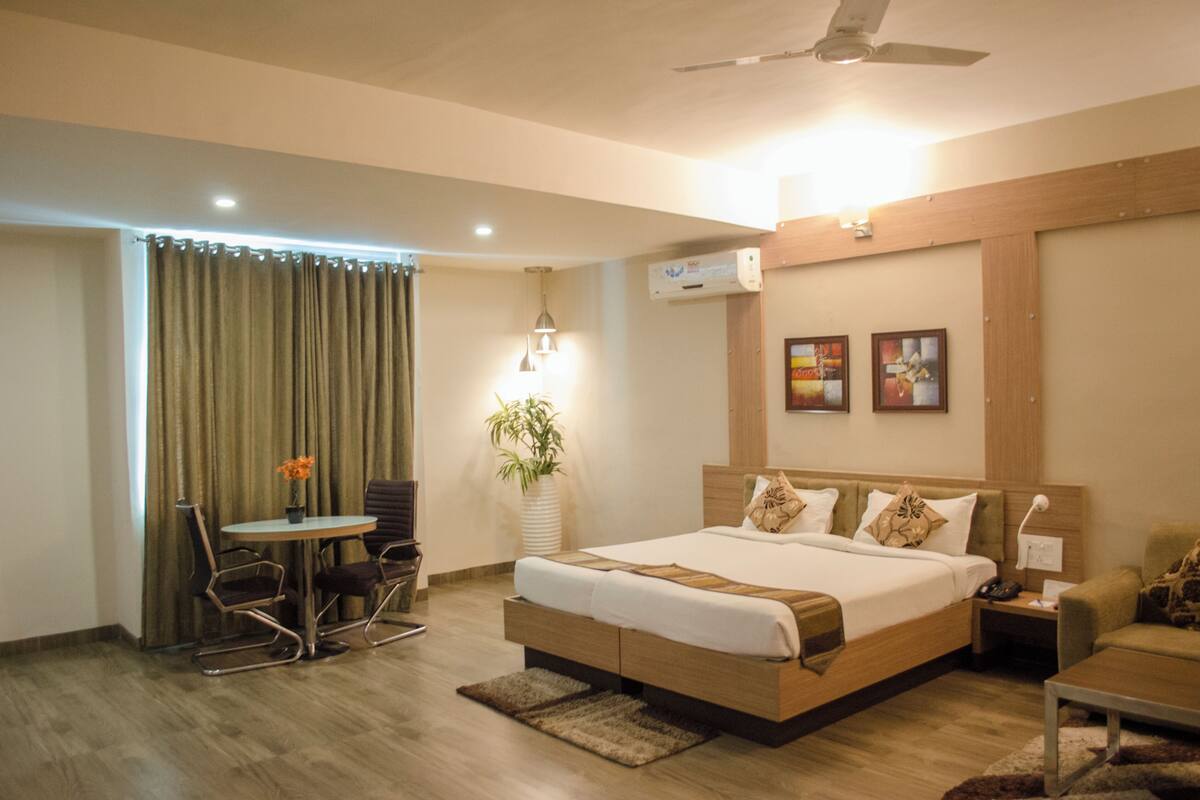 A hotel room with a bed, a desk, a chair, a table, a plant, and a ceiling fan.