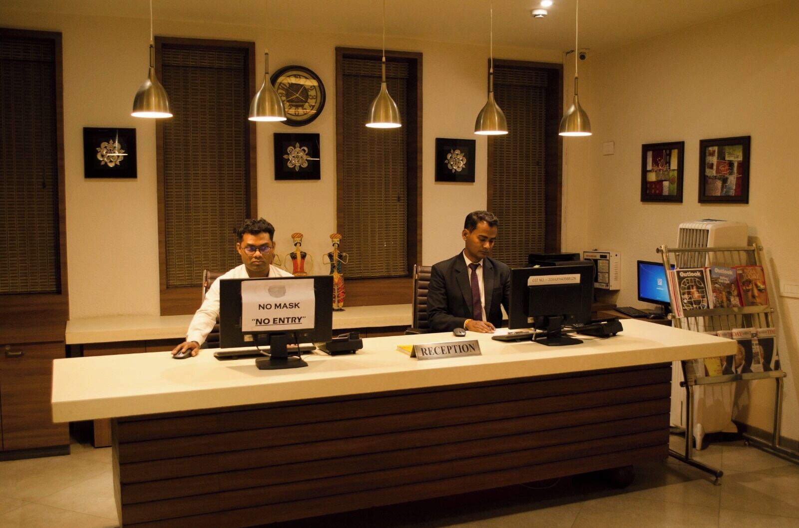 A reception desk with two staff members, a 'NO MASK' sign, and a 'NO ENTRY' sign.
