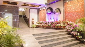 Vestíbulo de hotel con escaleras, paneles decorativos en la pared y plantas en macetas.