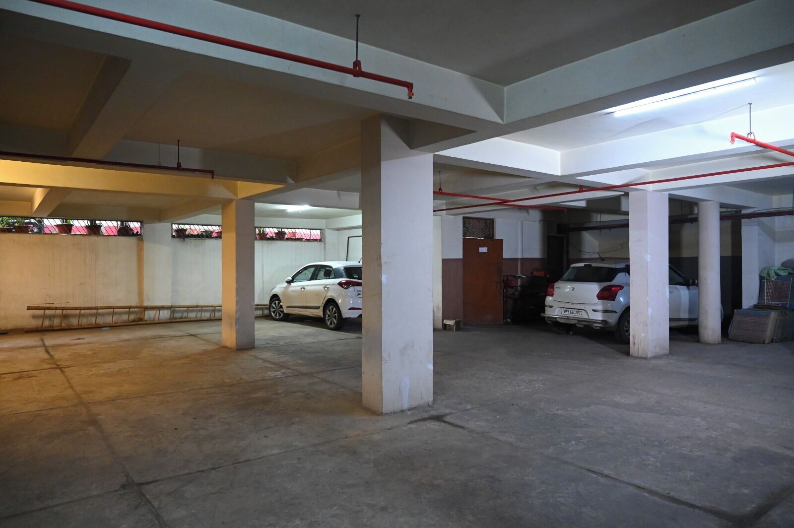 Un estacionamiento de varios niveles con pilares de hormigón, un coche blanco estacionado en el centro y una manguera contra incendios roja que recorre el techo.