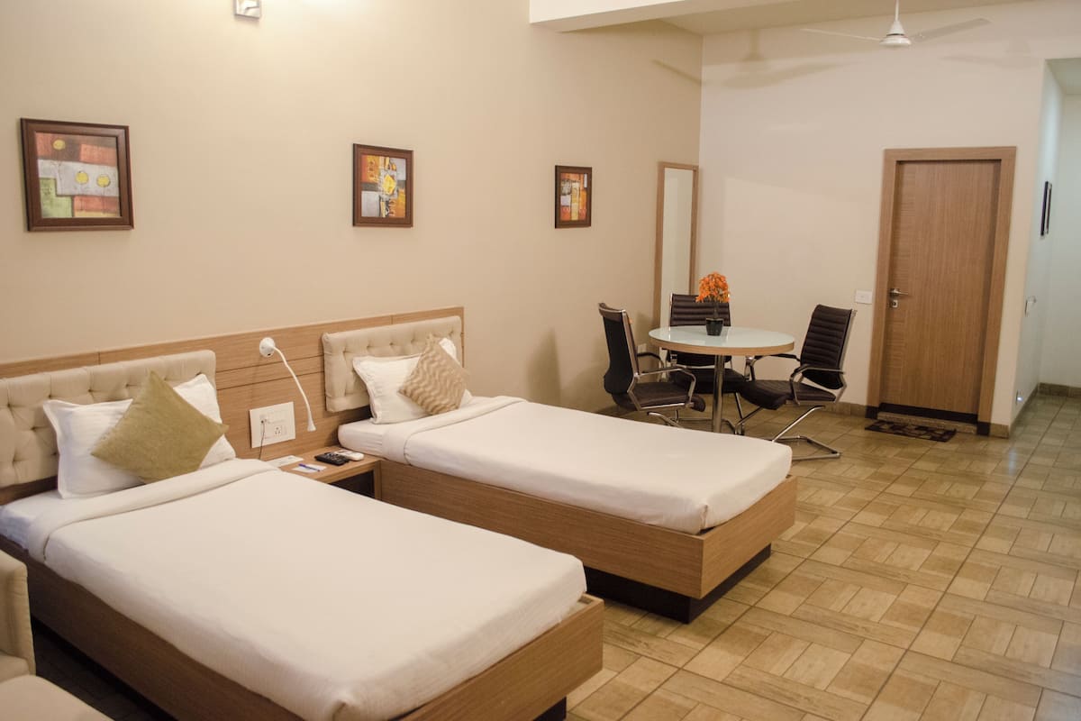 A hotel room with two single beds, a small table with chairs, a door, and framed artwork on the wall.