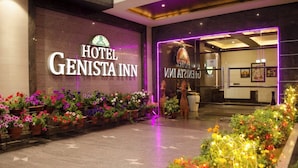 La entrada al Hotel Genista Inn, con un cartel llamativo, plantas en macetas y un área de recepción visible a través de las puertas de vidrio.