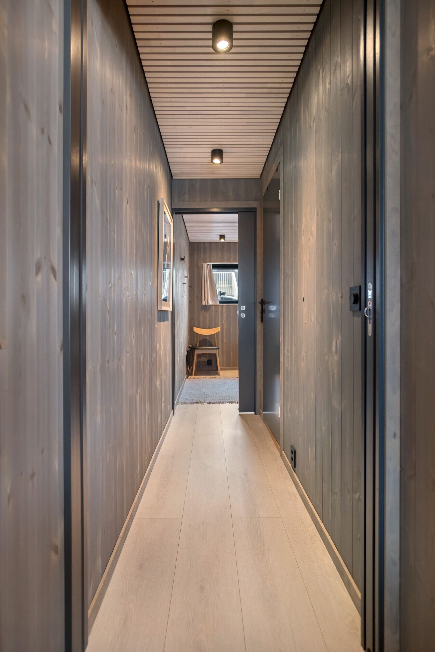 Ein Flur mit Holzwänden und Fliesenboden, der zu einem Zimmer mit Bett und Fenster führt.