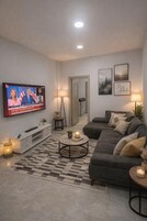Una sala de estar con una televisión mostrando un noticiero, un sofá, una mesa de centro y una lámpara.