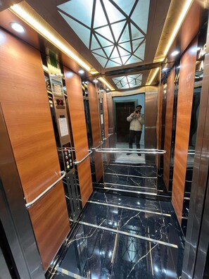 Interior de ascensor con paneles de madera, suelo de mármol y tragaluz.