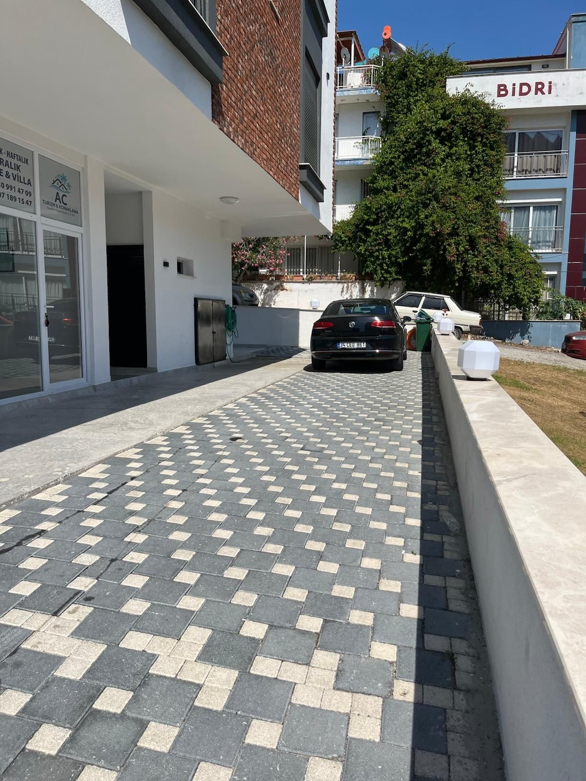 A paved driveway leading to a building with a sign for 'Bidri.'