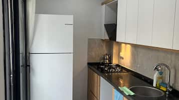 A compact kitchen with a refrigerator, stove, sink, and wooden cabinets.