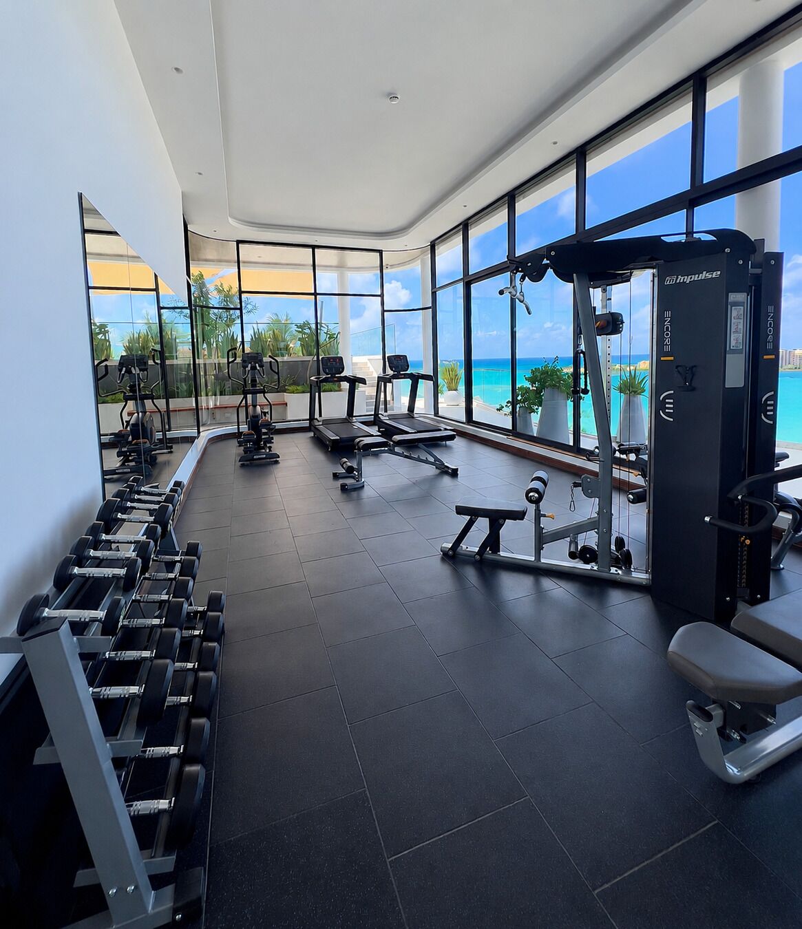 A gym with exercise equipment, large windows, and a view of the ocean.