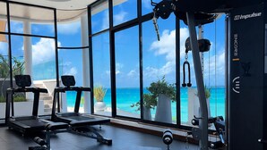 Ett gym med träningsutrustning, stora fönster och utsikt över havet.