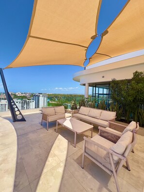 A rooftop terrace with outdoor furniture, a large shade canopy, and a city view. - Stylish 1BR in Nyali with Pool, WiFi & Beach Access (Mombasa)
