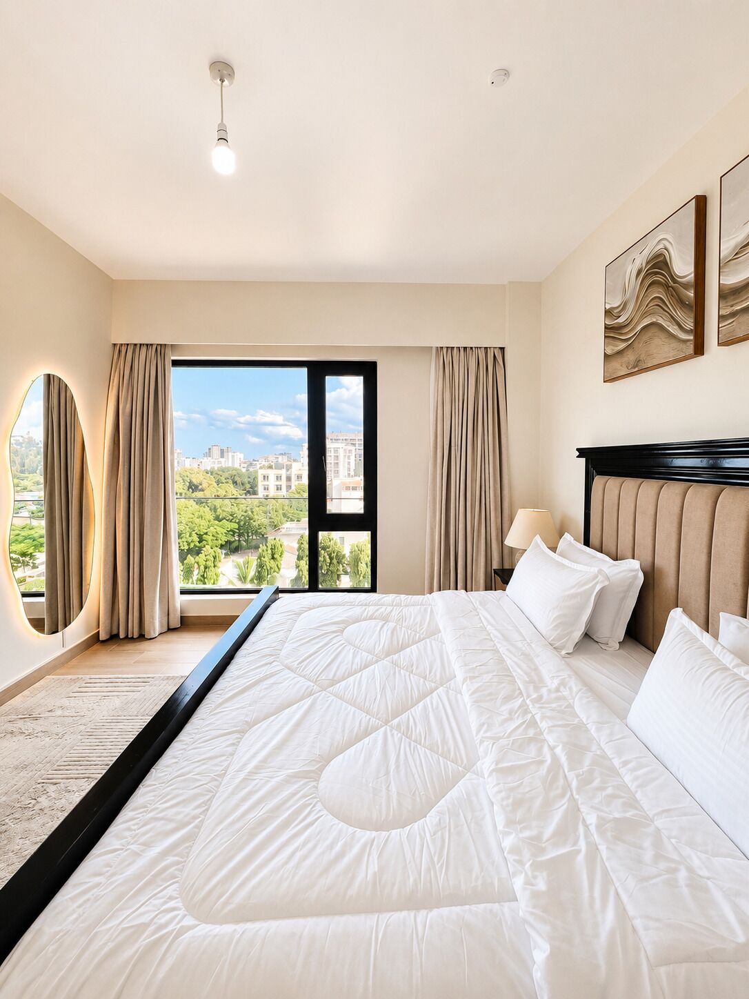 Een hotelkamer met een groot bed, uitzicht op een stadsbeeld, een ronde spiegel en een moderne lamp.