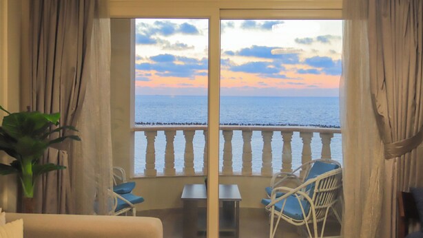 A balcony with a view of the sea, a chair, a table, and curtains. - Wide breathtaking Sea View Apartment (Alexandria Governorate)