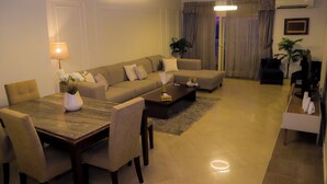 A modern living room with a sofa, a dining table with chairs, and a coffee table. There is a lamp on the table, a plant, and a framed picture on the wall. - Wide breathtaking Sea View Apartment (Alexandria Governorate)