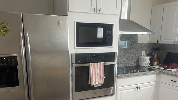 A kitchen with a stainless steel refrigerator, a microwave, an oven, and white cabinets. - Spacious 4-bedroom building with AC in amazing Pittsburg (Pittsburg)