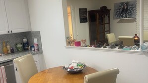A dining area with a round wooden table, beige chairs, a small bowl with items, and a kitchen in the background. - Spacious 4-bedroom building with AC in amazing Pittsburg (Pittsburg)