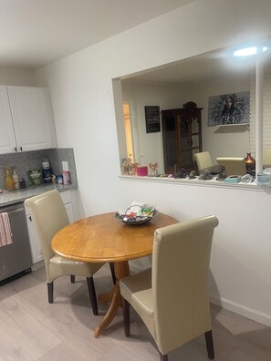 A dining area with a round wooden table, beige chairs, a small bowl with items, and a kitchen in the background. - Spacious 4-bedroom building with AC in amazing Pittsburg (Pittsburg)