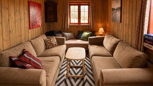 A cozy cabin interior with wooden walls, a sofa set, a small wooden table, and a window with curtains. - Spacious cabin with beautiful Geilo views (Hol)