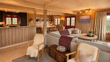 Een gezellig interieur van een chalet met een eethoek, een bank, schommelstoelen en uitzicht op de natuur.