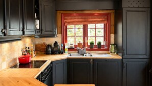 A kitchen with dark cabinets, a wooden countertop, a window with red curtains, and a view of greenery outside. - Spacious cabin with beautiful Geilo views (Hol)