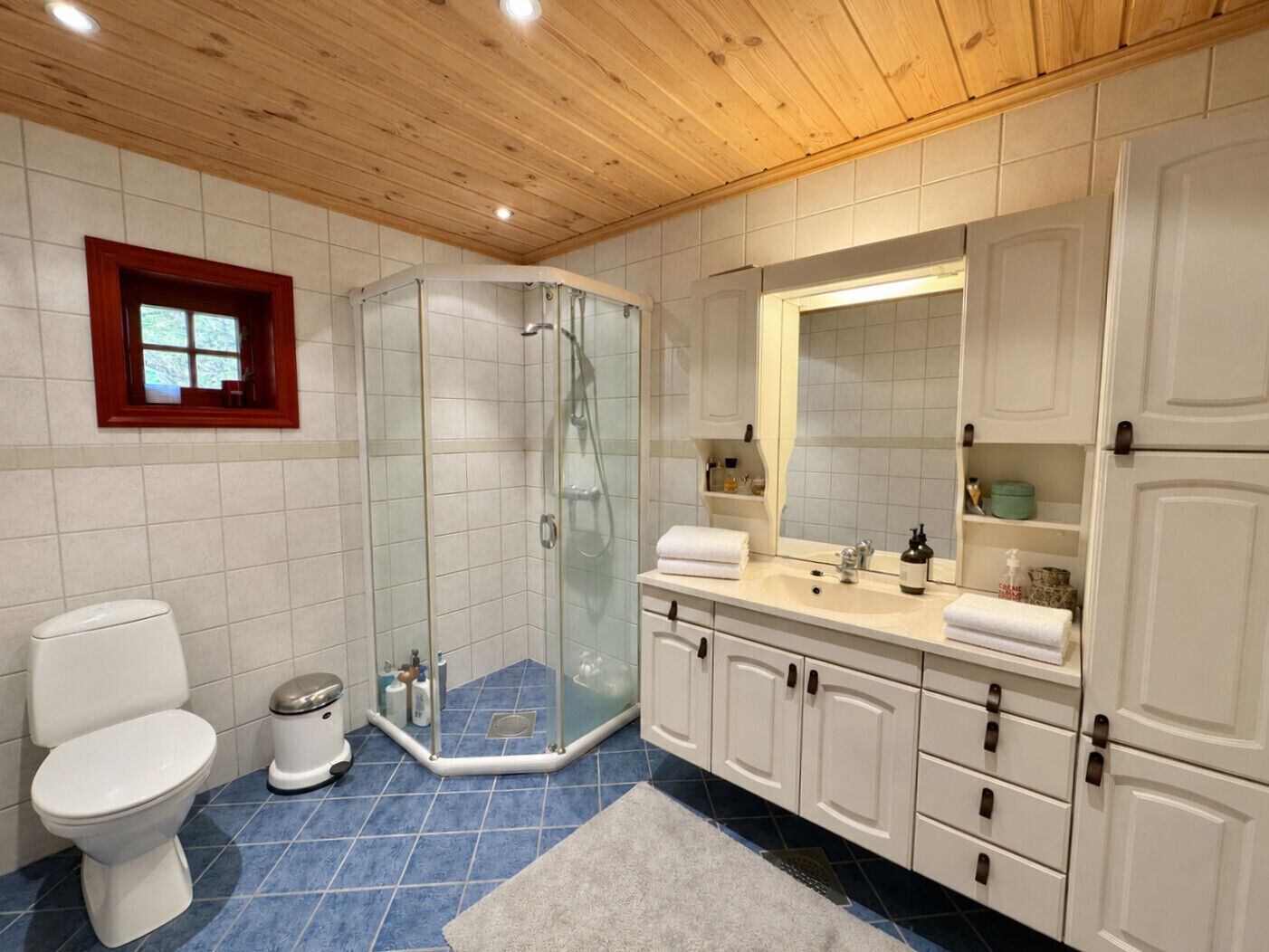 Een badkamer met een douchecabine van glas, een wit toilet, een wastafel met spiegel en witte kastjes.