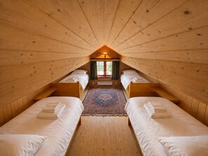 A room with two beds, a central window, and a wooden ceiling.