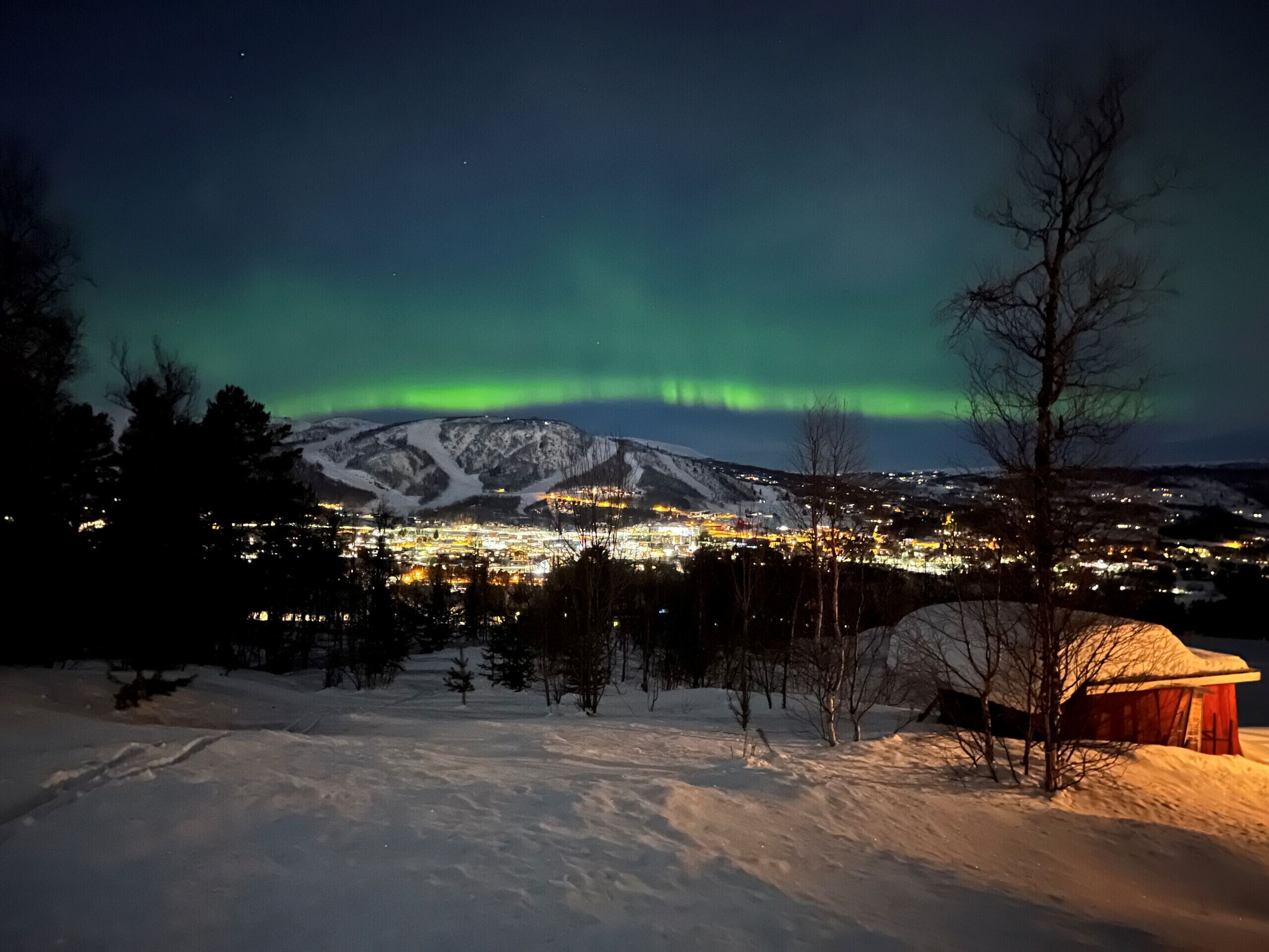 A snowy landscape with a mountain in the background and a lit building in the foreground.