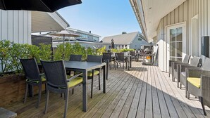 En utomhusveranda med bord och stolar, en grill och utsikt över de omkringliggande byggnaderna.