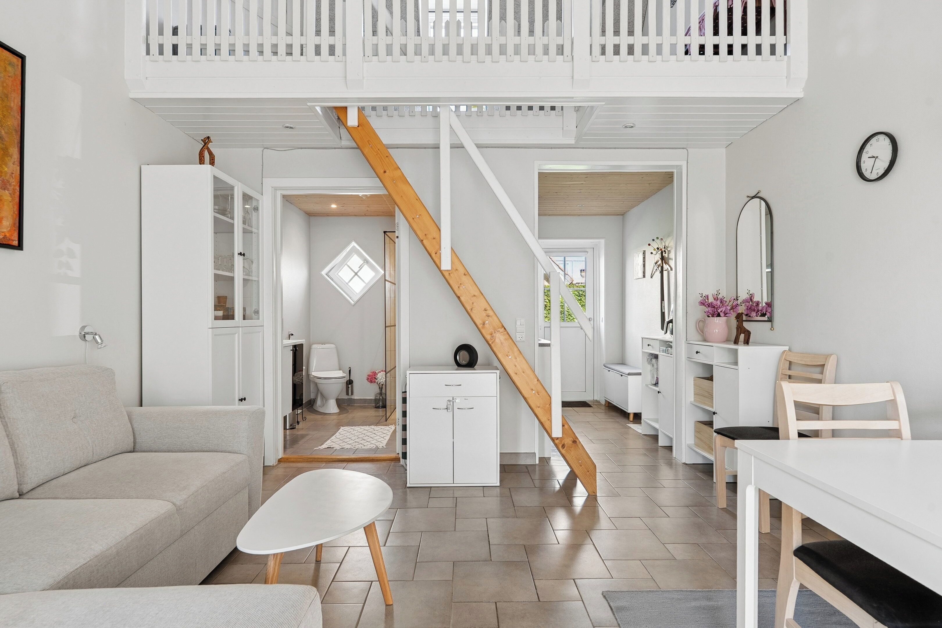 Um interior moderno com escada, mobiliário branco e uma sala de jantar.