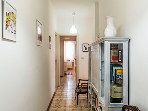 A hallway with a tiled floor, a cabinet with books, a chair, and a hanging light fixture. - Luna Verde by Interhome (Sanremo)
