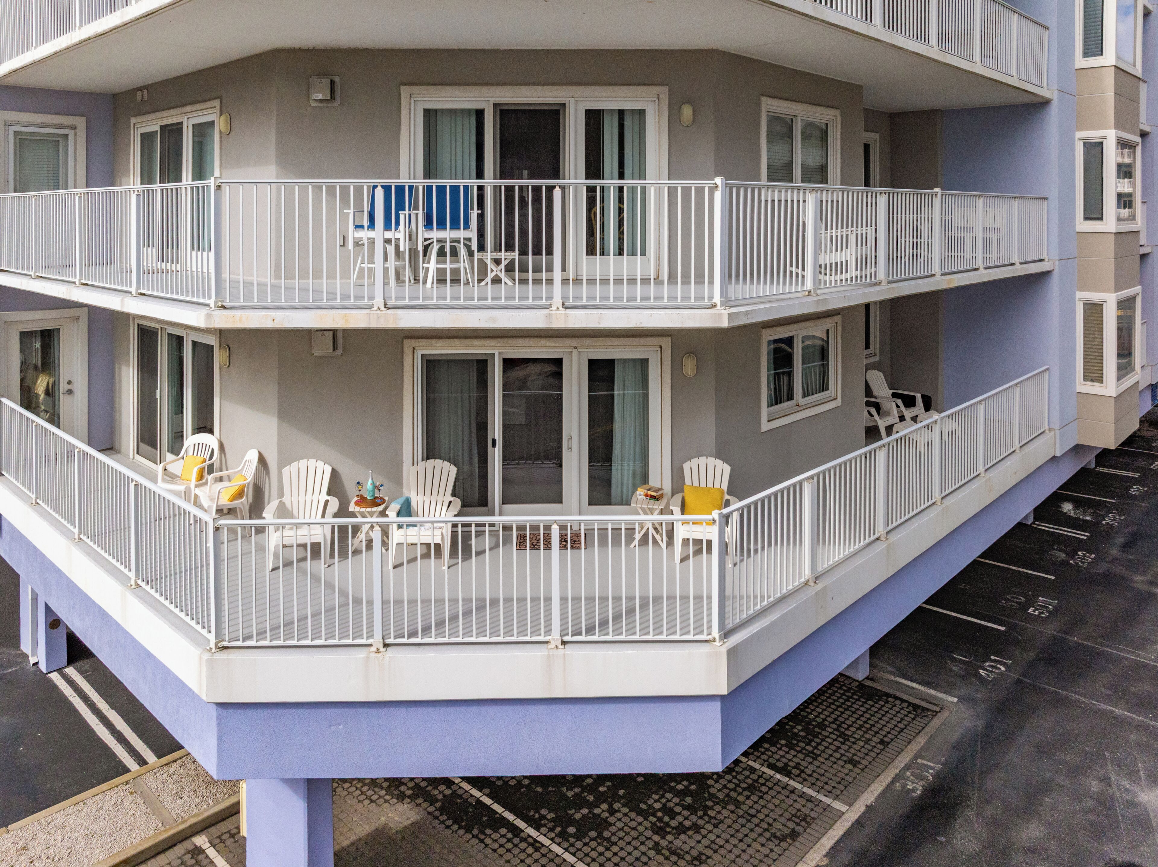 A multi-story residential building with balconies, white railings, and outdoor seating.
