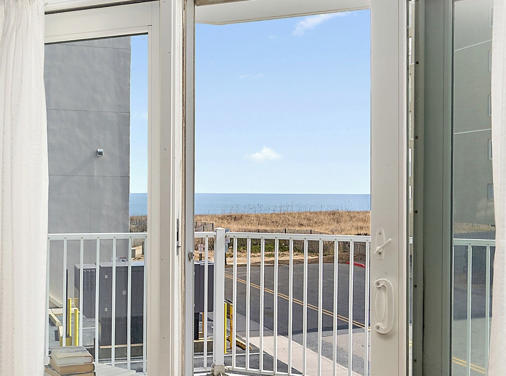 Une vue depuis un balcon doté d’une balustrade, avec un parking et une plage en arrière-plan.