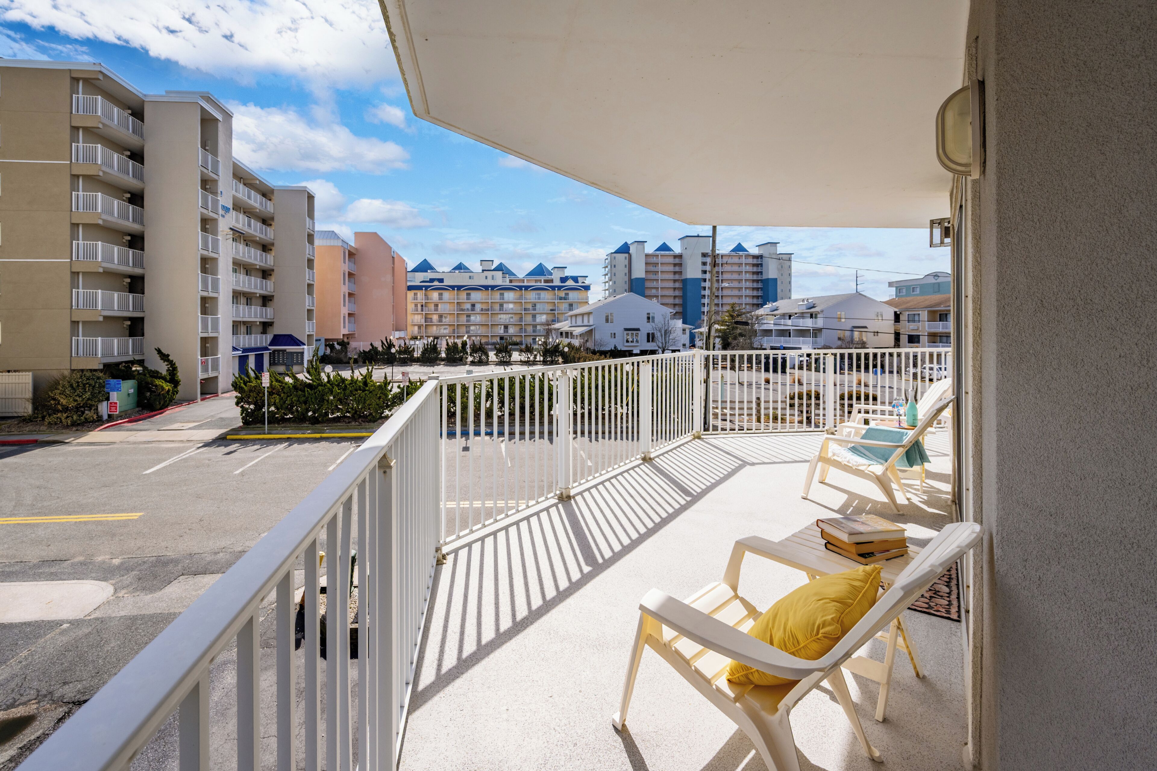 A balcony with white railings, a white chair with a yellow cushion, and a table with a book.