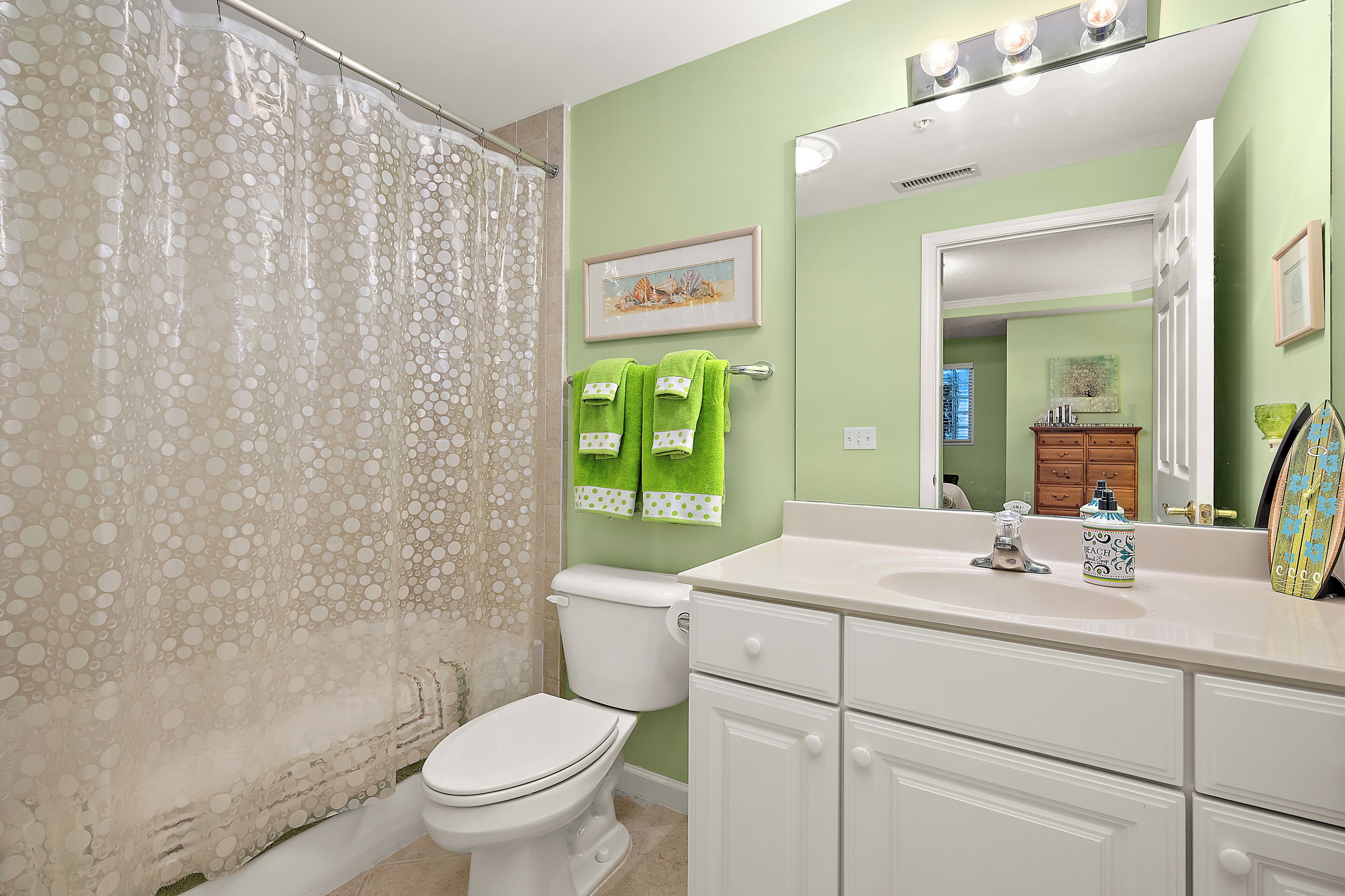 A bathroom with a toilet, a shower curtain, a sink, a mirror, and a cabinet.