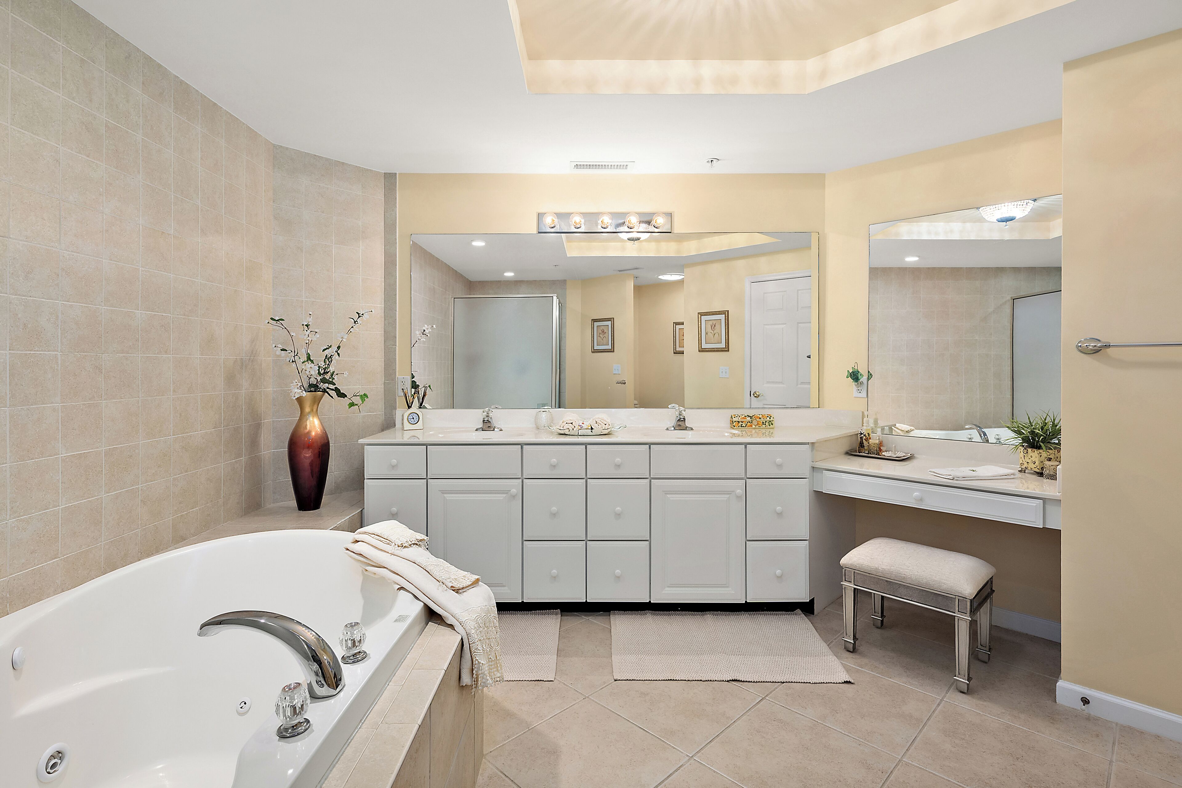A modern bathroom with a large bathtub, double vanity with mirrors, and a bench.
