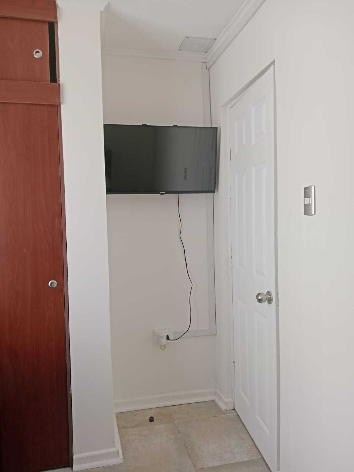 Una habitació amb una porta blanca, una porta marró i una televisió penjada a la paret.