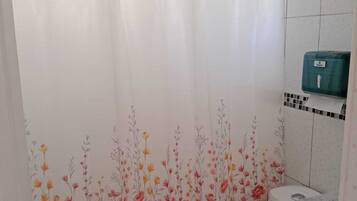 A bathroom with a shower curtain, toilet, and a soap dispenser.
